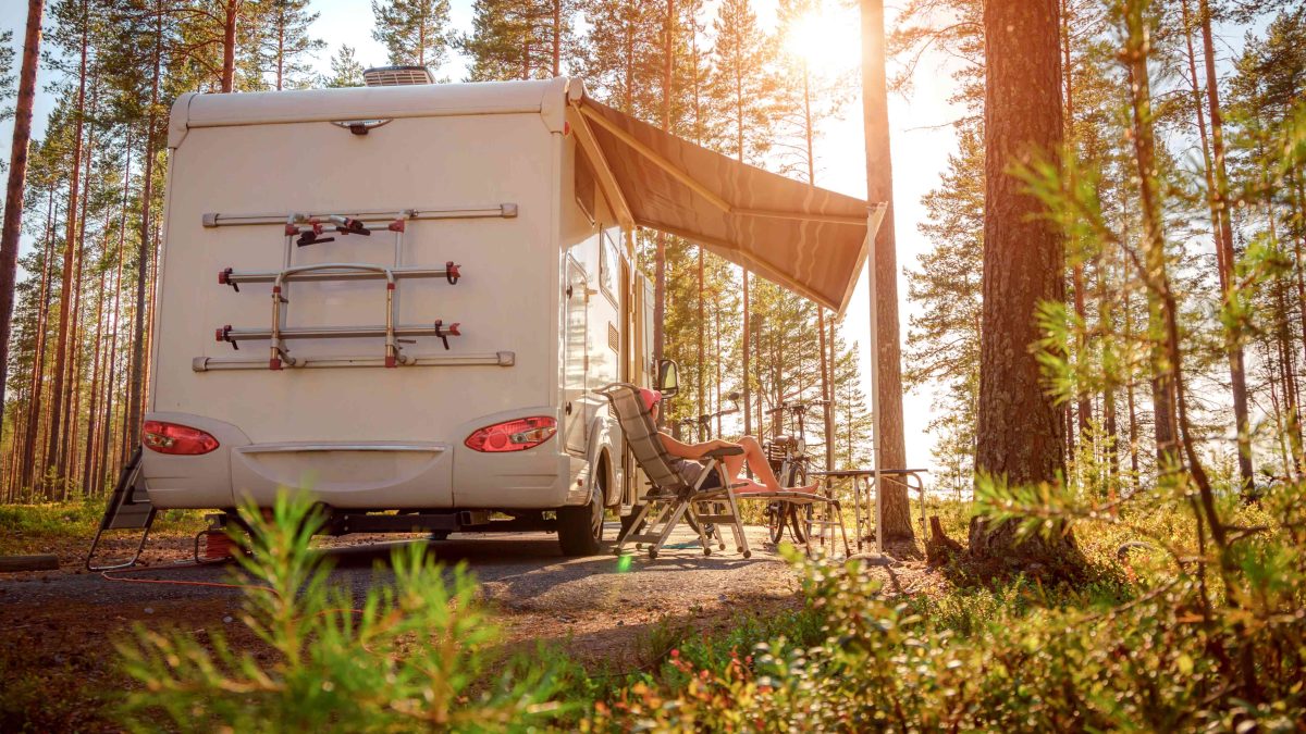 Ein Wohnmobil unter Bäumen mit entsprechender Campingausstattung