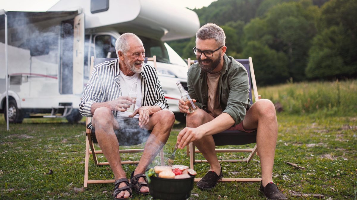 Zwei Männer grillen vor einem Wohnmobil.