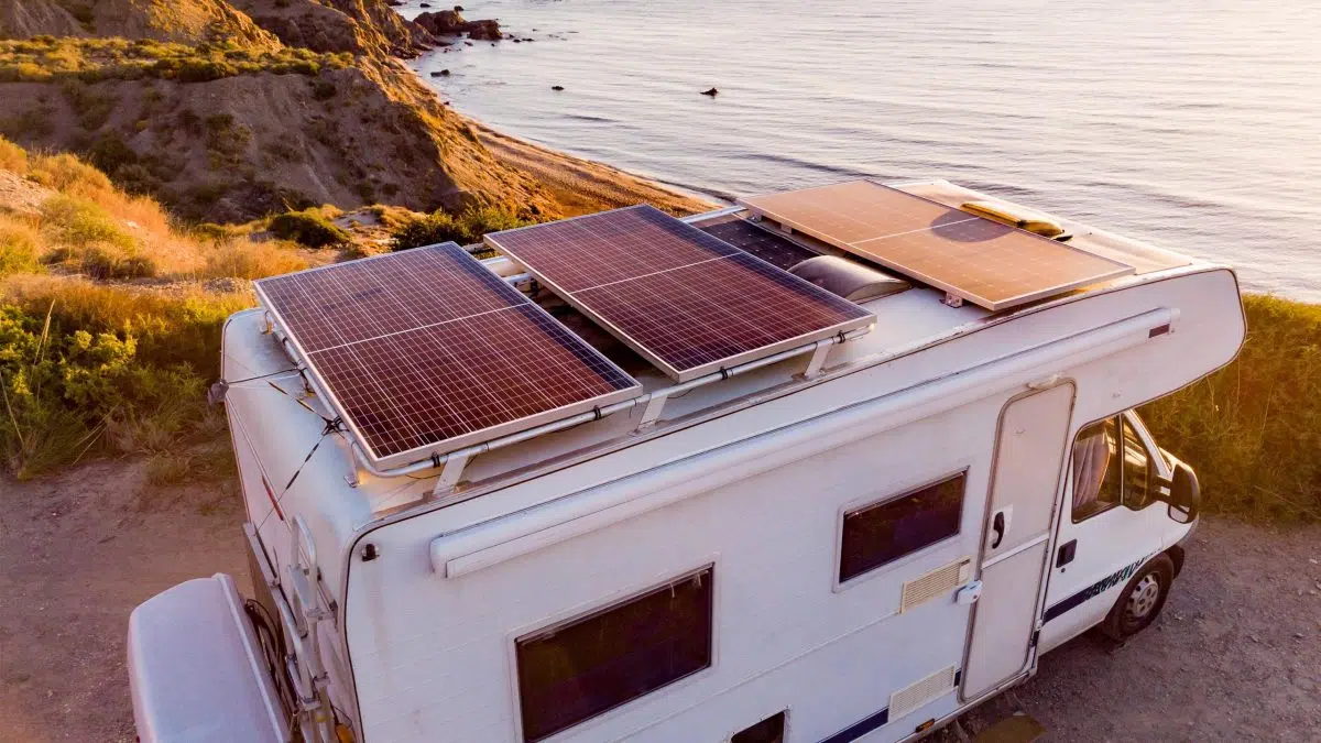 Ein Wohnmobil mit Solarpanelen steht bei Sonnenuntergang an einer Küste.